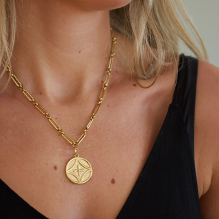 Gold tone necklace with a large decorative pendant worn by a person in a black top, Can You Shower, Swim, and Sweat in Water Resistant Jewelry?