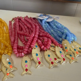 Three beaded fish necklaces in yellow, pink, and light blue, each with multiple strands of round beads and a gold fish-shaped pendant decorated with colorful rhinestones, displayed on a light surface.