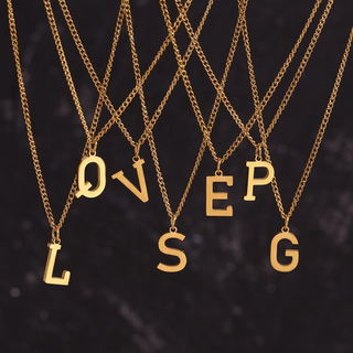 Six gold letter necklaces spelling out 'LOVE SEP G' hang in a fan-like arrangement against a dark textured background.