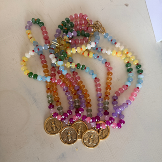 A set of colorful beaded necklaces with gold-toned coin pendants, arranged on a light beige surface.