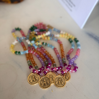 A set of colorful beaded necklaces with gold coin charms, arranged on a light marble surface.