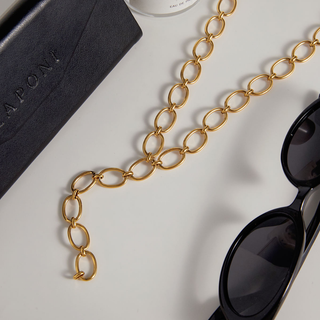 Gold chain necklace with black sunglasses on a light gray surface