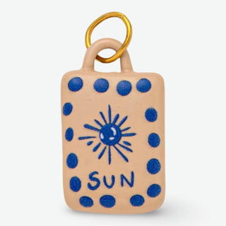 Handcrafted ceramic sun charm with blue sun design on cream background and stainless steel jump ring