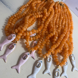 Orange Maris Fish Beaded Necklace with white fish charm and gold-tone accents on orange glossy beads