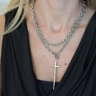 Close-up of a person wearing a layered necklace with a cross pendant.