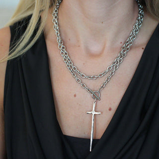 Close-up of a person wearing layered necklaces with a prominent cross pendant.