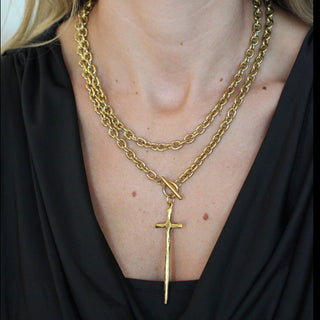 Close-up of a person wearing a gold chain necklace with a cross pendant.