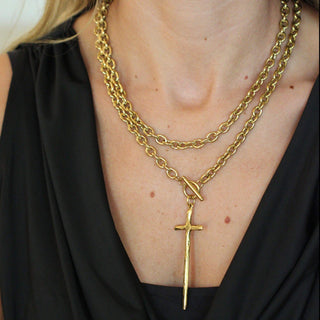 Person wearing a gold chain necklace with a cross pendant on a black top.
