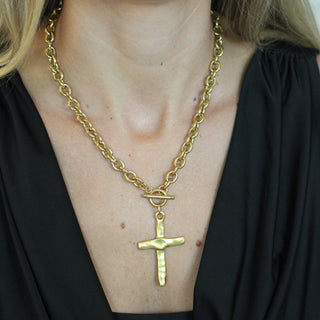Gold chain necklace with a cross pendant worn by a person against a black background