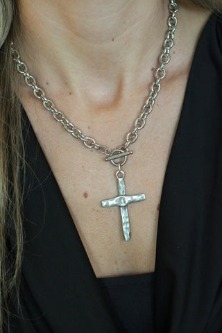 Silver chain necklace with a cross pendant on a person wearing a black top.