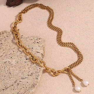 Gold chain necklace with pearl pendants on a textured beige surface