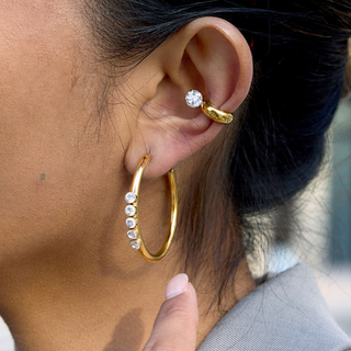Halo Ear Cuff in polished gold with a single round clear stone, worn above a large gold hoop earring