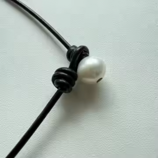 Hometown Pearl Choker with dark leather cord knotted beside a single white freshwater pearl drop