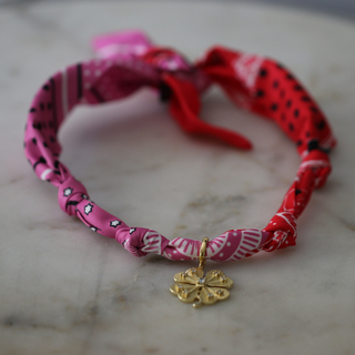 Lucky Charm Scarf Necklace with a twisted pink and red patterned fabric band and a small gold four-leaf clover pendant