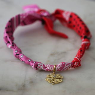 Lucky Charm Scarf Necklace with a twisted pink and red patterned fabric band and small gold clover pendant
