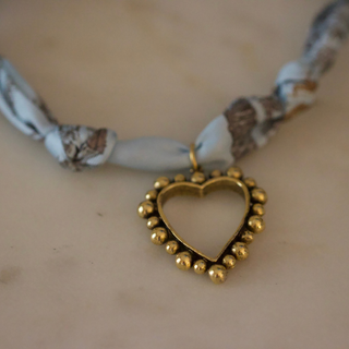 Skyline Heart Scarf Necklace with a pale blue and gray patterned fabric tie and an open gold-tone heart pendant bordered with beads.
