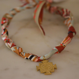 Terra Benedict Necklace with a multicoloured patterned fabric cord and ornate gold-tone cross-shaped pendant.