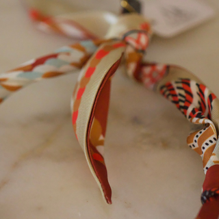 Terra Benedict Necklace with a flowing rust, cream and orange patterned scarf, tied into a decorative fabric design.